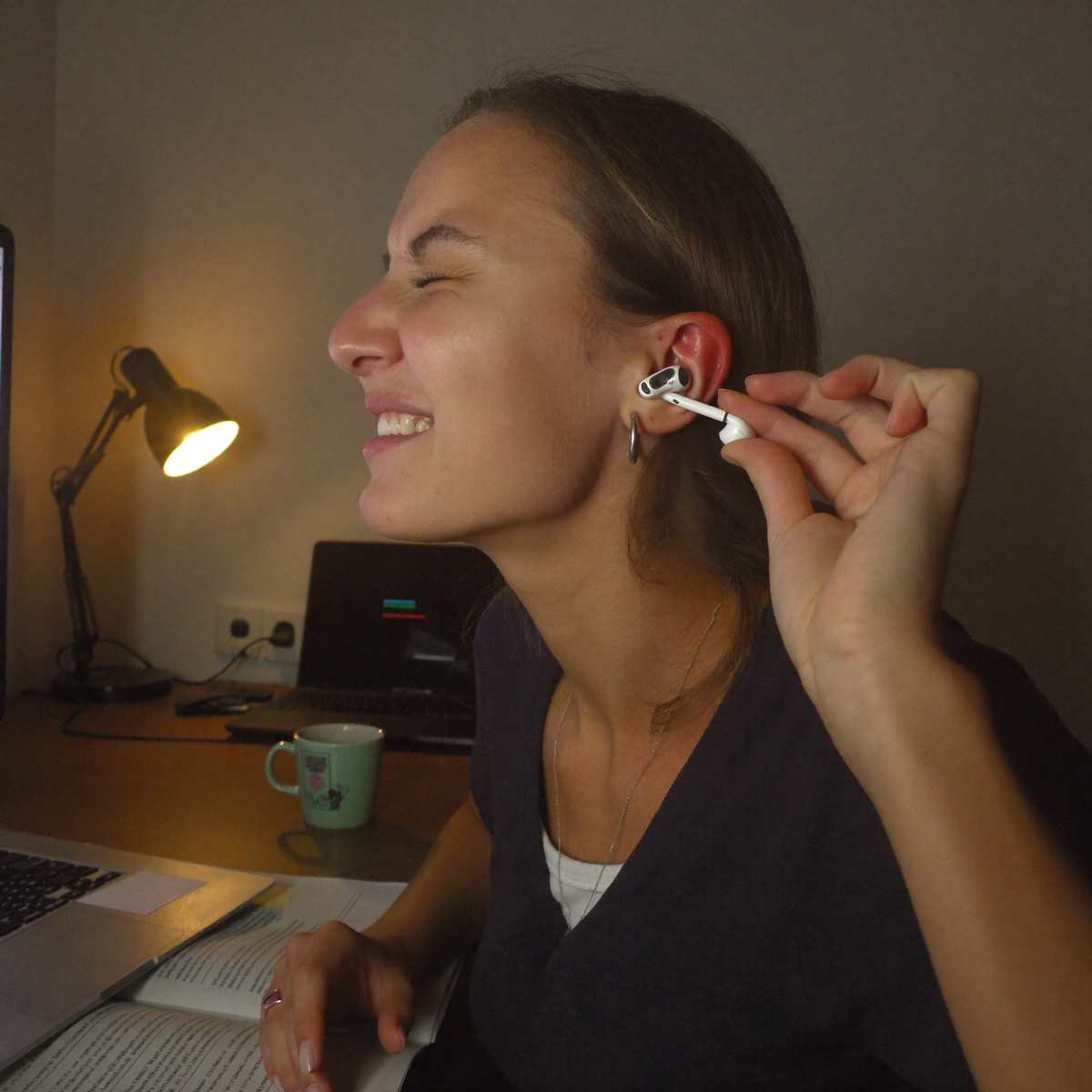 Woman at her desk wincing while pulling a sealed in-ear earbud out of her irritated ear